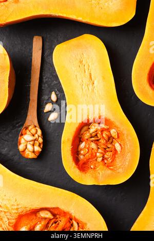 Sliced squash with seeds and wooden spoon on black textured surface. Autumn cooking concept with pumpkin and organic ingredients Stock Photo