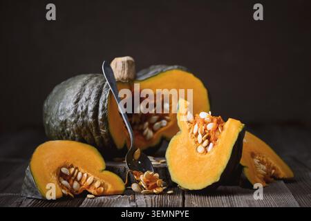 Fresh pumpkin wedges beside whole squash in warm moody lighting. Rustic autumn composition with harvest vegetables and organic food styling Stock Photo