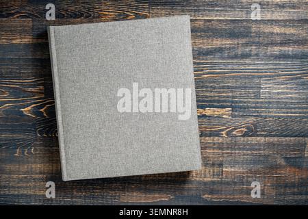 Grey linen photo album or book on dark wooden background, close up. Top view of a blank gray fabric hardcover notebook or photobook placed on a dark r Stock Photo
