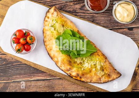 Freshly baked Italian calzone pizza served with fresh rocket and dipping sauces Stock Photo