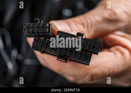 Computer power supply connectors in hand, Close up of a hand holding black ATX 24 pin and CPU power connectors for a PC hardware assembly Stock Photo