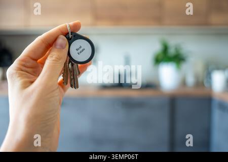Woman holding house keys with real estate keychain inside modern apartment interior. Property ownership and housing market concept for real estate Stock Photo