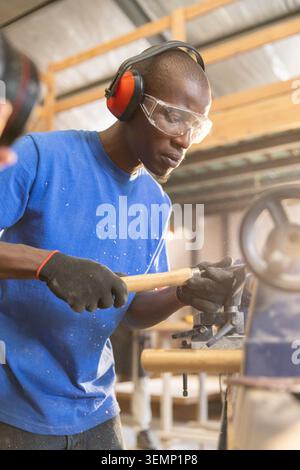 Mid adult African American man striking chisel with hammer on workbench wearing hearing protection Stock Photo