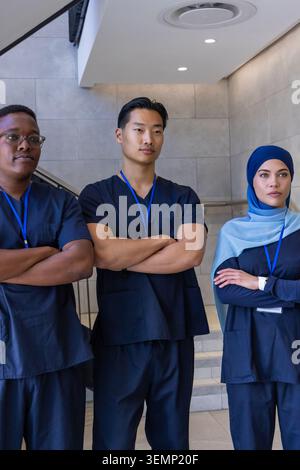 Diverse healthcare team posing with arms crossed in hospital wearing navy scrubs and blue lanyards Stock Photo