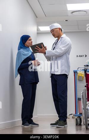 Diverse medical colleagues in navy scrubs and white coat discussing scan on tablet near X-RAY sign Stock Photo
