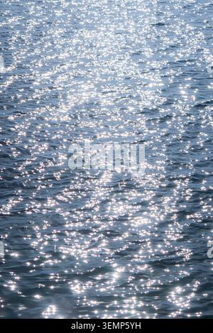 Sparkling sunlight reflecting on calm blue water surface with gentle ripples and waves Stock Photo