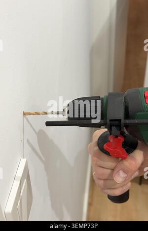 Close up of green drill bit pulled back from drilled hole in white plaster wall Stock Photo