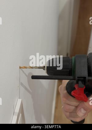 Macro of corded drill with masonry bit and depth gauge boring into white wall Stock Photo