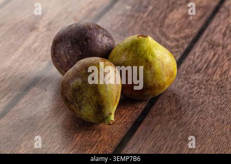 Three ripe figs with purple and green hues resting on dark wooden surface, healthy organic fruit, closeup food photography, natural lighting, healthy Stock Photo