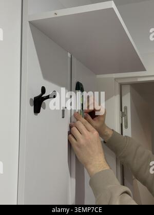 Hands using green spirit level on white coat rack panel during furniture installation Stock Photo