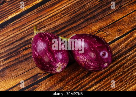 two fresh purple eggplants with green stems lying on textured wooden surface. vibrant violet skin with white streaks. natural lighting highlights glos Stock Photo