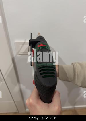 Top down view of corded electric drill held vertically against white wall near light switch Stock Photo