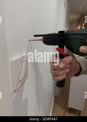 Hand drilling hole in white wall near light switch with corded electric drill Stock Photo