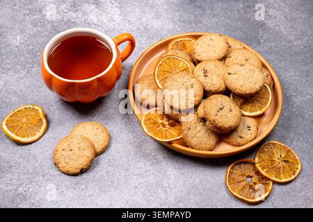 Warm tea in a pumpkin shaped mug creating a soothing autumn atmosphere, served with homemade cookies and decorative dried orange slices on a textured Stock Photo