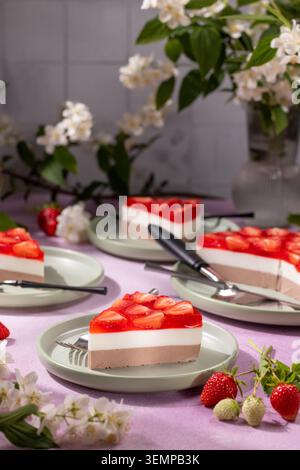 Strawberry triple mousse cake slices with vibrant red jelly atop layers of vanilla and chocolate mousse, served on green plates with fresh strawberrie Stock Photo