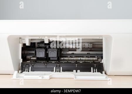 Close-up interior view of a home printer with the front tray open, exposing black ink cartridges, paper feed rollers and internal mechanisms for offic Stock Photo