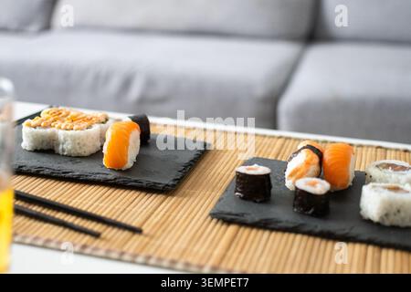Close-up of assorted sushi, nigiri, and maki rolls served on black slate plates over a bamboo placemat. Stock Photo
