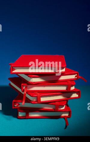 Stack of red notebooks against a bold blue background Stock Photo