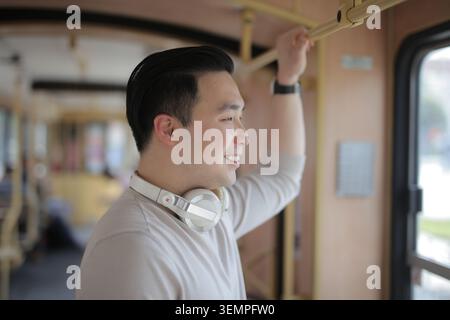 Smiling man with headphones looking out bus window Stock Photo