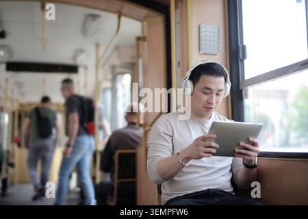Young Asian man using a tablet on public transit Stock Photo