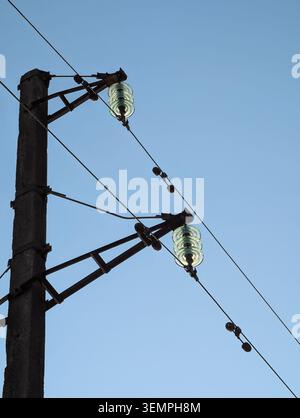 High voltage power line with glass Insulators. Low angle view of glass suspension insulators & electrical wires on a concrete utility pole, clear sky. Stock Photo