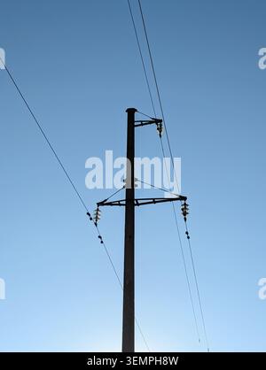 Silhouette of high voltage utility pole against clear blue sky. Minimalist vertical shot of a concrete power line pole and glass insulators. Stock Photo
