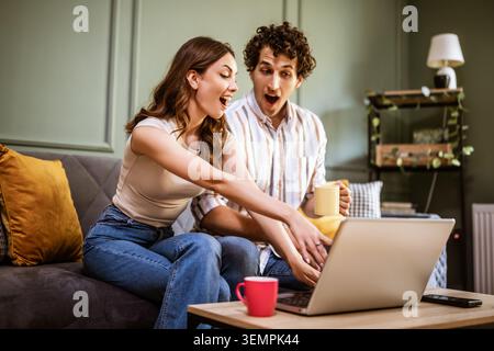A couple enjoys a relaxed afternoon indoors, reviewing information on a laptop while sharing conversation and coffee. Stock Photo