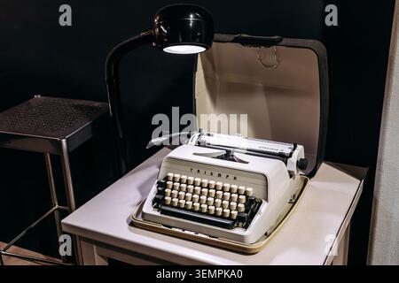 Amsterdam, Netherlands - April 19, 2026: Vintage Triumph portable typewriter displayed on a desk under a reading lamp, showcasing classic writing tech Stock Photo