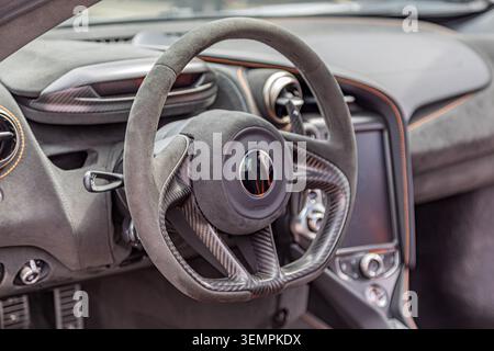 Close-up of luxury car steering wheel, featuring carbon fiber center with soft suede rim, metallic accents, sleek dashboard design, dark gray tones, s Stock Photo