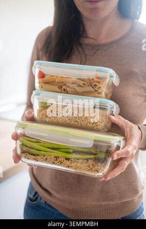 Close-up of a woman holding stacked glass meal prep containers filled with healthy homemade food, including pasta, brown rice, quinoa, and fresh veget Stock Photo