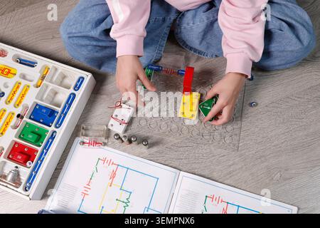 Child hands close-up assembling electronic circuit components on plastic grid base plate. Educational STEM laboratory activity for physics science Stock Photo