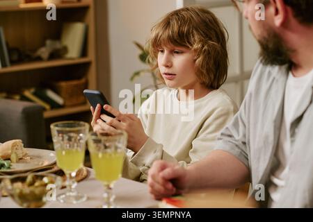 Boy Using Smartphone during Family Lunch at Home Stock Photo