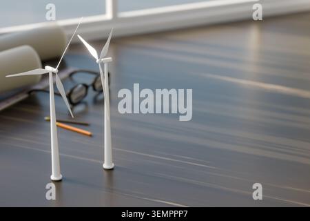 3D render of wind turbine models on a wooden table with blueprints, glasses, and pencils. Concept of renewable energy engineering, sustainable project Stock Photo