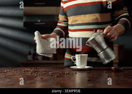 A man in a striped sweater is poured coffee from a geyser coffee maker into a white cup. It's an authentic vintage Italian coffee maker, a 1950s and 1 Stock Photo