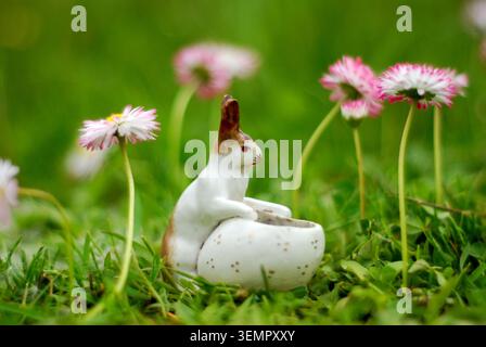 Decorative composition, porcelain Easter bunny of the Russian Empire period on a floral field and green background of nature. Close-up front view. Stock Photo