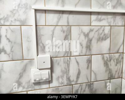 A junction box with wiring runs along the tiled wall in a domestic space showing electrical connections and installations. Stock Photo
