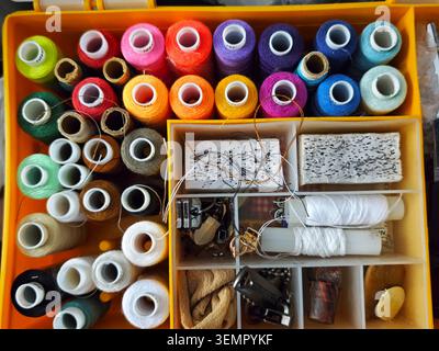 Various threads in different colors are neatly arranged in a box along with sewing supplies on a table during the afternoon. Stock Photo