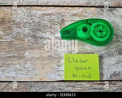 A sticky tape roller sits on a wooden surface next to a small note that says clear your mind. The setting is a home or office desk with natural light Stock Photo
