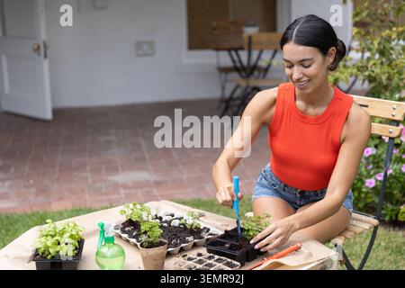 Woman gardening using trowel at seedling trays on kraft-paper table on brick patio, copy space Stock Photo