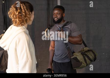Diverse friends in sportswear talking in gym by rings, man holding duffel, water bottle, copy space Stock Photo