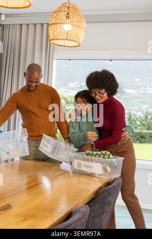 Diverse family with child sorting recyclables at dining table with labeled bins and egg carton Stock Photo