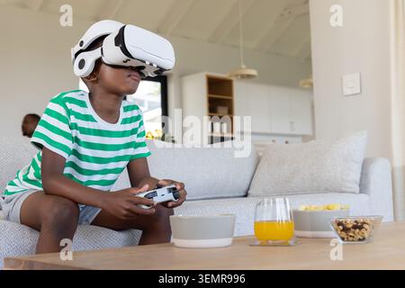 African American family watching preteen boy using white VR headset and holding controller on couch Stock Photo