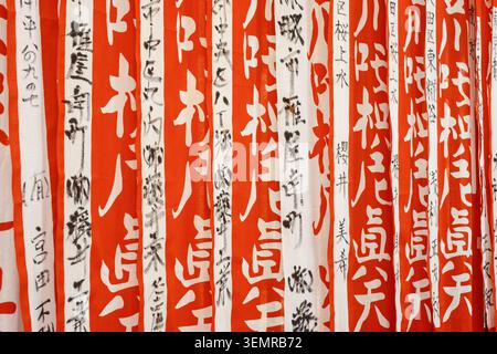 Full-frame abstract texture view of multiple hanging red prayer banners featuring black painted vertical calligraphy text, Tokyo, Japan Stock Photo