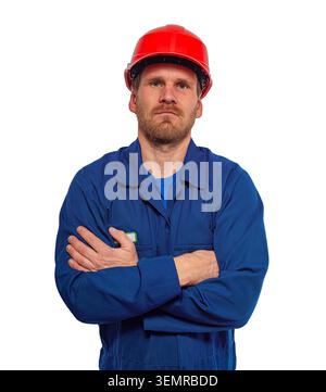 Worker stands with his arms crossed wearing a blue jumpsuit and a red hard hat against a white background. Stock Photo