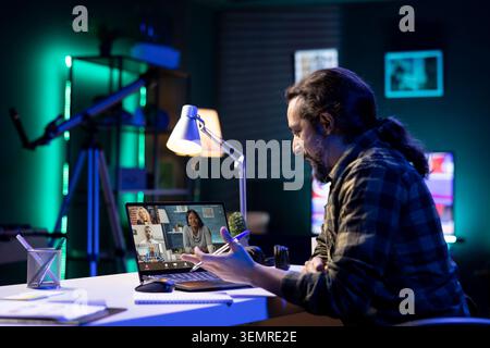 Young guy participating in an online meeting with a group of people seen on laptop screen, they are communicating, comparing notes, and actively involved in video conference from different locations. Stock Photo