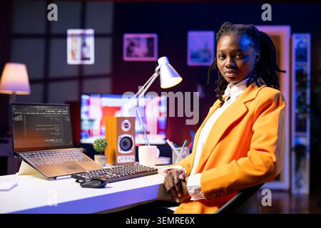 Portrait of programmer at desk typing code on laptop, developing software programs, entering commands, african American woman at home fixing errors in application, implementing new features. Stock Photo