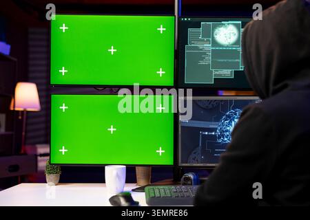 Hooded hacker installing spyware using isolated screen PC and AI to secretly gather data about victims. Stock Photo