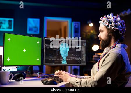 Software engineer with EEG headset starting mind upload on green screen PC, trying to gain bionic powers, with IT admin using high-tech neuroscientific gear and mockup computer. Stock Photo