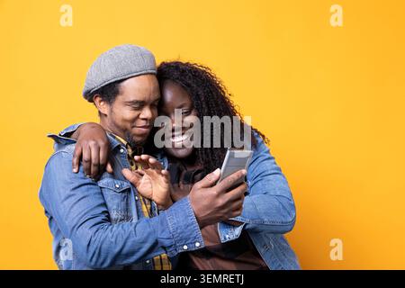 African American young couple having fun together with videos on social media, looking at something online on smartphone, cute husband and wife feeling happy in front of camera. Stock Photo