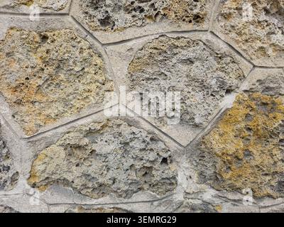 Close-up of a rustic stone wall texture featuring porous, volcanic or coquina stones in shades of grey and yellow, held together by clean concrete mor Stock Photo